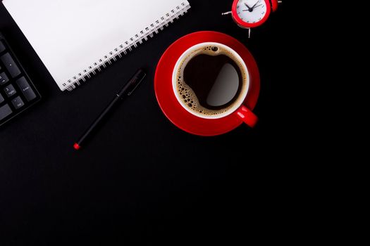 red cup of coffee, pen, glasses, alarm, plant, phone, and paper on a black background as workplace top view space for text