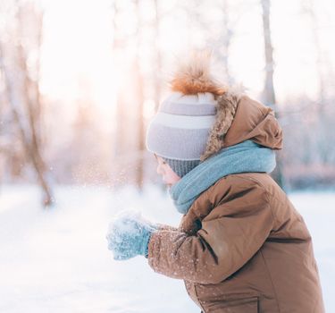 A boy blows snow off his hands winter lifestyle . Winter painting. Snow Park. Cold. Happy childhood