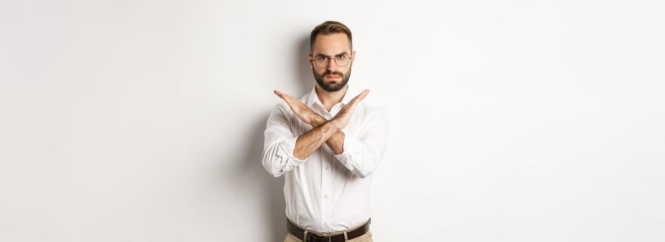 Angry businessman frowning and showing cross, stop you, telling no and prohibit something, standing over white background.