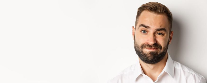 Emotions and people concept. Headshot of skeptical man with beard, grimacing and looking doubtful, standing displeased against white background.