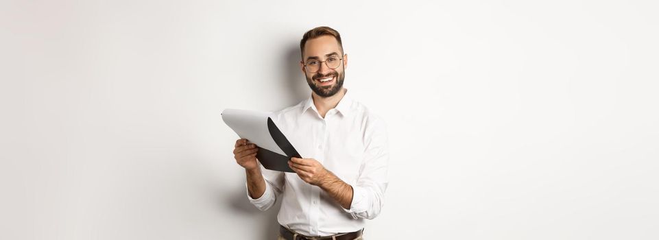 Employer looking satisfied at CV, reading document and smiling, standing over white background.