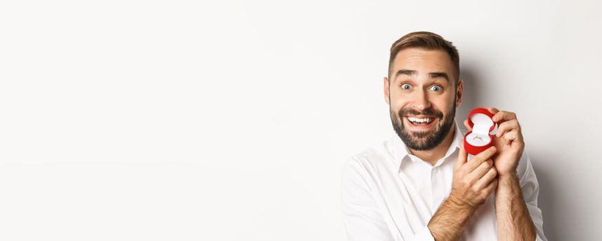 Close-up of handsome guy making proposal, looking hopeful and showing wedding ring, asking marry him, white background.