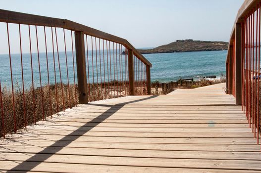 Wooden footpath on a beach entrance near Porto Covo, Portugal. Peach tree island in the background..