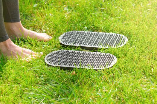 legs of a woman standing on the grass next to sadhu yoga boards with nails outdoors. Close up