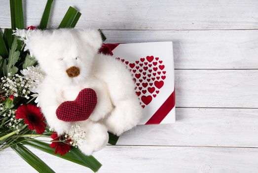 Valentine's day gift, teddy bear with a heart, a box of pralines and a bouquet of flowers on the bed early in the morning. High quality photo