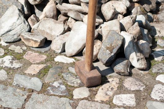 a gardener in dirty work clothes and boots holds a two-bladed iron hammer for working with stones. High quality photo