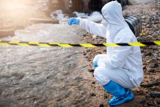 Ecologist sampling water from the river with test tube, Scientist or Biologist in a protective suit and protect mask collects sample of waste water from industrial for analyze, problem environment