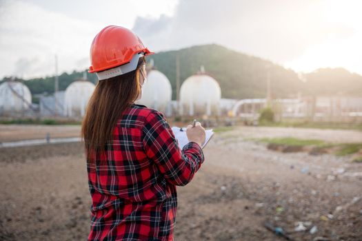 Petroleum Engineers. Happy Asian worker woman in oil chemical industry working visual inspection list on clipboard in plant, do Action of worker standing write safety checklist which is clipped