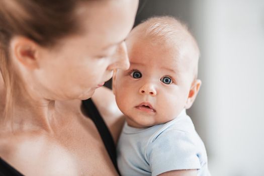 Portrait of sweet baby resting in mothers arms, looking at camera. New mom holding and cuddling little kid, embracing child with tenderness, love, care. Motherhood concept.