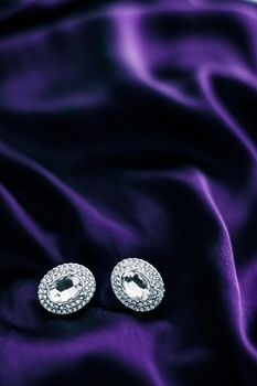 Jewellery brand, elegant fashion and bridal luxe gift concept - Luxury diamond earrings on dark violet silk fabric, holiday glamour jewelery present