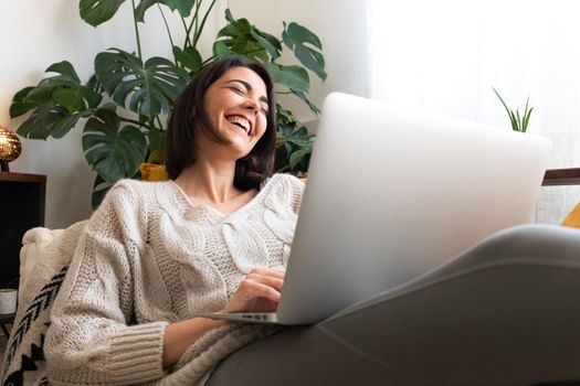 Young caucasian woman laughing at home while using laptop. Watching funny online videos. Technology and lifestyle concept.