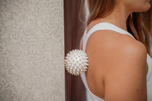 Athletic slim caucasian woman doing thigh self-massage with a massage ball indoors. Self-isolating massage.