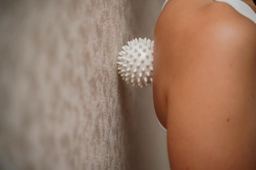 Athletic slim caucasian woman doing thigh self-massage with a massage ball indoors. Self-isolating massage.