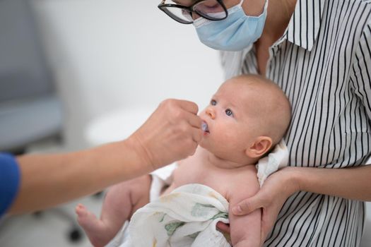 Pediatrician administring oral vaccination against rotavirus infection to little baby in presence of his mother. Children health care and disease prevention.