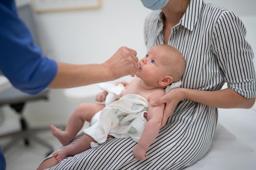 Pediatrician administring oral vaccination against rotavirus infection to little baby in presence of his mother. Children health care and disease prevention.