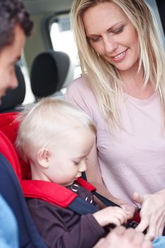 Making sure our son is safe. A mother and father helping their child in a baby seat for the car