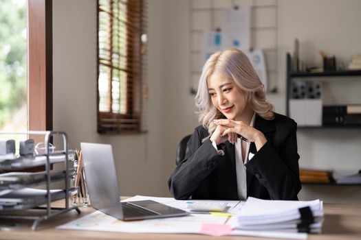 Young finance market analyst working at sunny office on laptop while sitting at wooden table. Businesswoman analyze document graphs and diagramm on notebook screen.