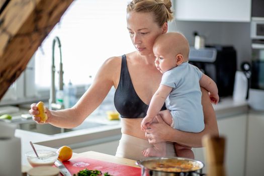 Woman cooking while holding four months old baby boy in her hands.
