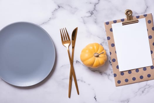 Autumn flat lay with blank tablet, ceramic plate and pumpkin on marble background top view.