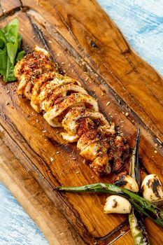 Spicy sliced grilled squid with green pepper and garlic on a wooden serving board