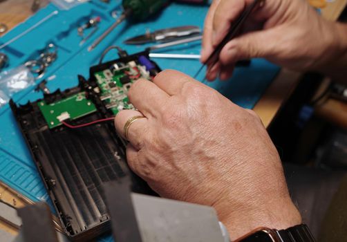 The hands of a man who uses tweezers to take apart a faulty portable charger