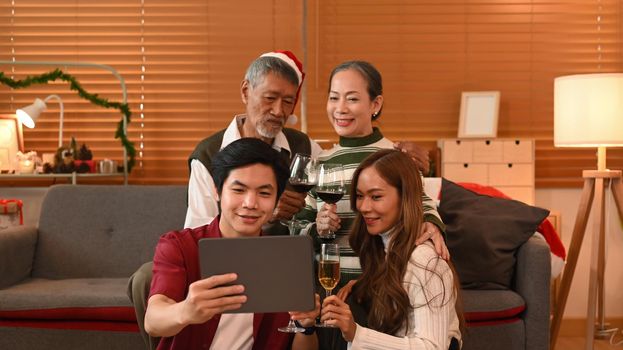 Happy family making video call over digital tablet, sitting in room decorated for celebrating New year and Christmas festive.