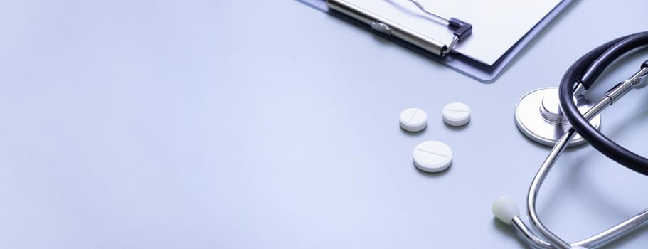 Banner with stethoscope, pills and tablet at doctor's workplace on colored background with copy space.