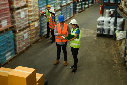 Warehouse worker and manager checking order details on a tablet while standing between retail warehouse full of shelves.