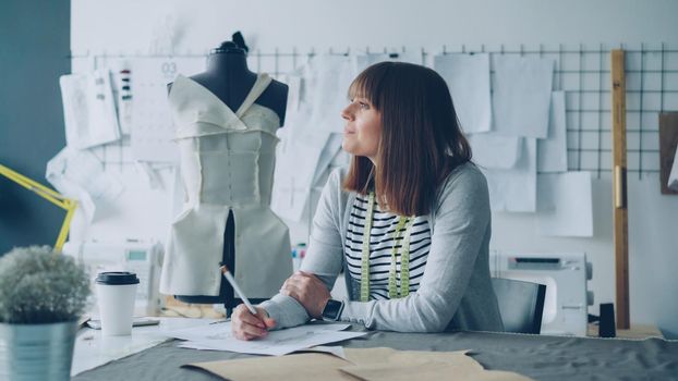 Attractive clothing designer in small start-up business is drawing sketches for women's clothes and thinking about next fashion show. Inspiration and creative thinking concept.