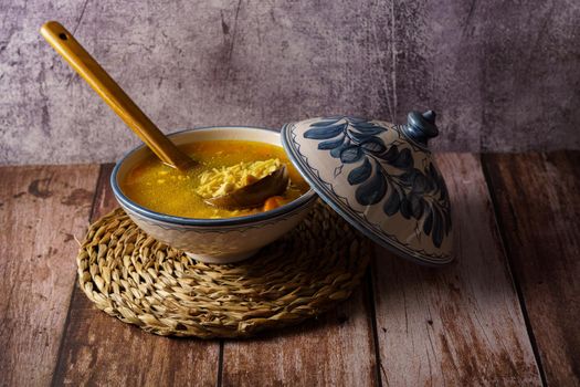 white and blue soup tureen with chicken noodle and vegetable soup with a wooden spoon