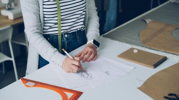 creative clothing designer concentrated on drawing sketch of trendy women's garment on piece of paper with pencil. Creating fashionable clothes concept.