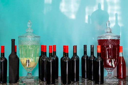 Many bottles of wine and 2 jugs with homemade drinks, tinctures and compotes on a blue background. Rustic style, homely cozy atmosphere, house wine. Home cafe concept, cozy atmosphere, copy space