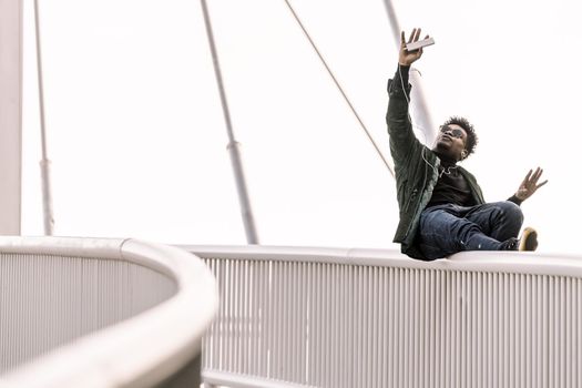 happy black man posing for selfie on smartphone while listen music in earphones or making a funny video call outdoors in the city, technology and lifestyle concept using internet electronic device