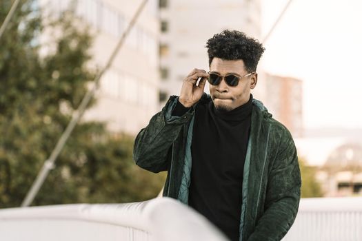 handsome young african black man with green jacket and sunglasses walking by the city, lifestyle concept