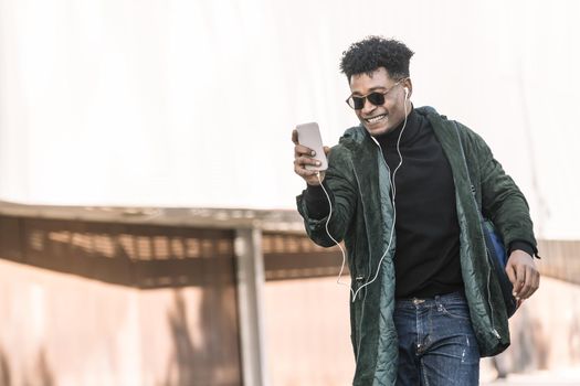 black young man with earphones making a video call with a mobile phone, technology and lifestyle concept using internet electronic device outdoors