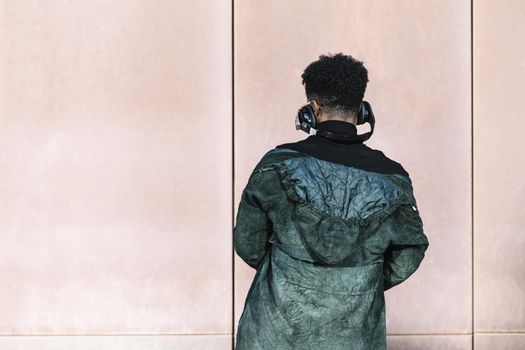 back view of a black man with headphones to listen music in front of a wall, technology and lifestyle concept