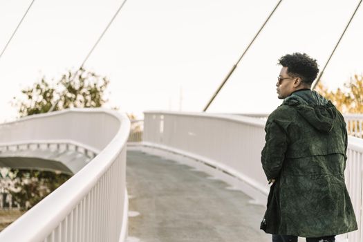 view from behind attractive young black african man with cool casual wear and sunglasses walking on a modern bridge in the city, lifestyle concept