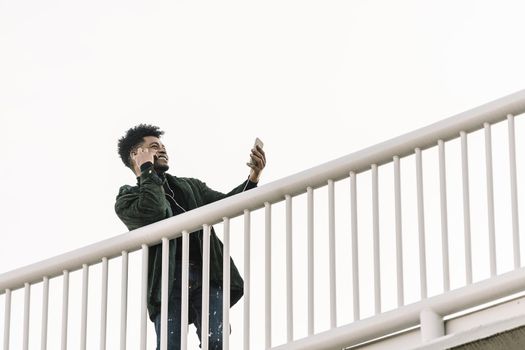 smiling black man with smartphone listening music in earphones or making video call outdoors in the city, technology and lifestyle concept using internet electronic device
