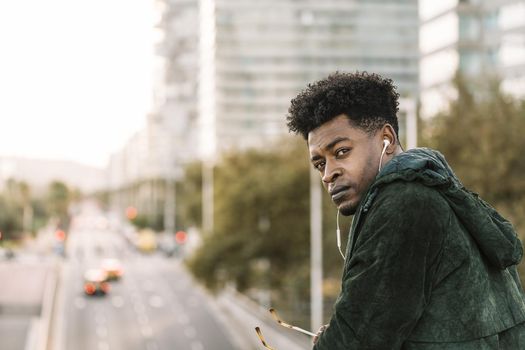 attractive young black african man with green jacket listening music with white earphones in the city, lifestyle concept