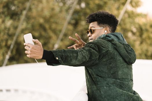 cool young african black man taking a selfie with smartphone and earphones while poses for the photo, city lifestyle and technology concept using internet electronic device
