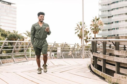 cool smiling african black man texting message on the phone while walks in a park outdoors in the city, lifestyle and technology concept, copy space for text