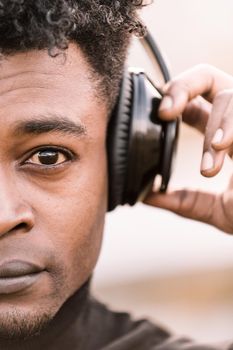 vertical half head portrait of a serious african black man listening music with a hand touching the headphones, technology and lifestyle concept