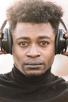 vertical portrait of a serious african black man listening music with the hands touching the headphones, technology and lifestyle concept
