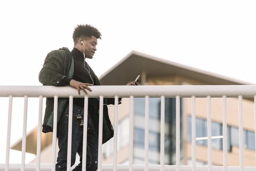 happy young african black man in earphone walking at sunny city and enjoying to listen to music on his smart phone, technology and lifestyle concept using internet electronic device