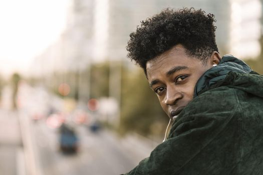 attractive young black african man with green jacket listening music with white earphones, city lifestyle concept