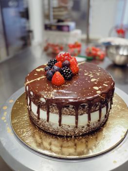 hand of chef toppig a choco cake with gold and berries in the lab