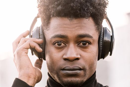 portrait of a serious african black man listening music with a hand touching the headphones at sunset, technology and lifestyle concept