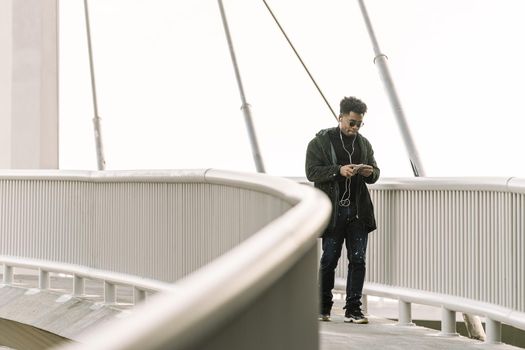 black man walks around looking at his smartphone while listen music in earphones in the city, technology and lifestyle concept using internet electronic device