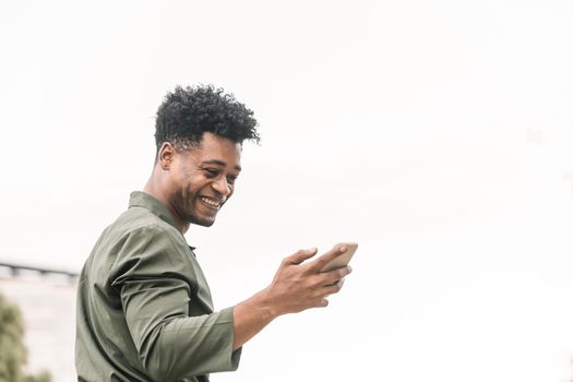 portrait of a cool young african black man texting a message and looking the phone in white background, lifestyle and technology concept, copy space for text