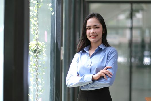 Young confident smiling Asian business woman leader, successful entrepreneur, elegant professional company executive ceo manager. Asian business woman is standing in office with arms crossed